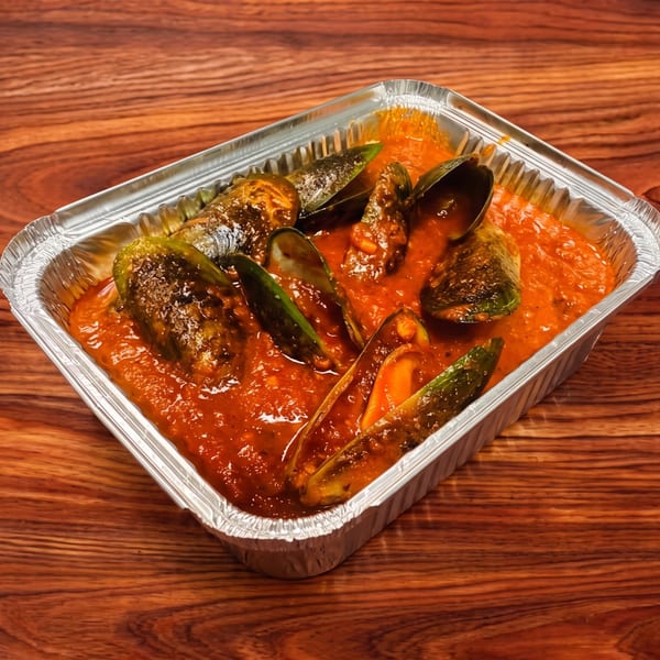 Mussels in a rich red sauce, served in a silver foil takeout container on a wooden table.