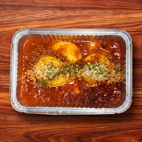 Ravioli in red sauce with cheese and herbs in a silver takeout container on a wooden table.
