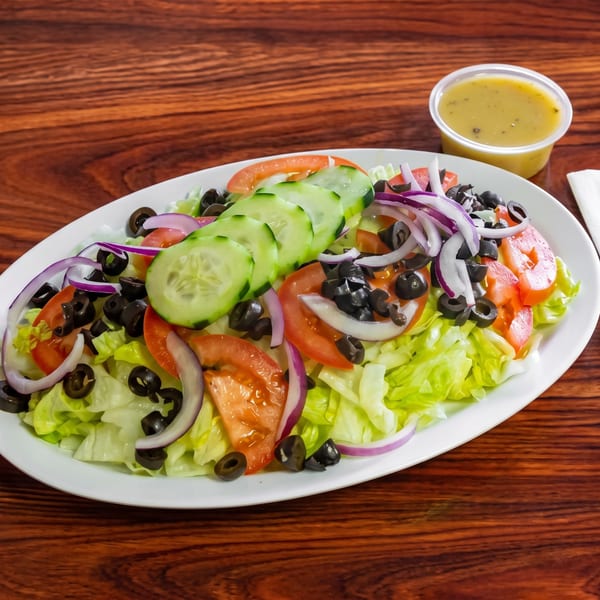 Fresh garden salad with lettuce, tomatoes, cucumbers, red onions, and black olives, with dressing on the side.