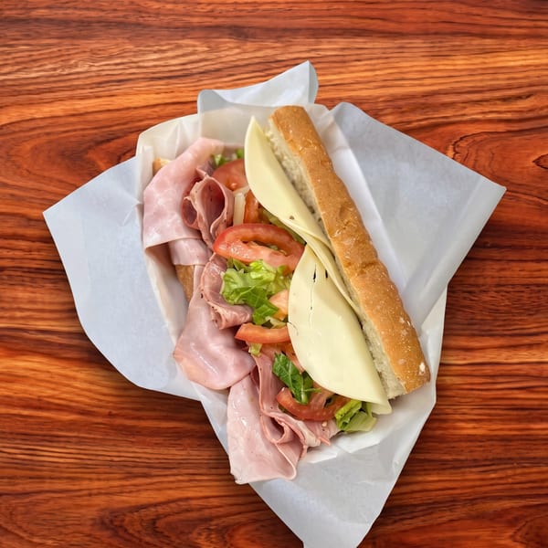 A large sub sandwich with ham, cheese, lettuce, and tomatoes, wrapped in paper on a wooden table.